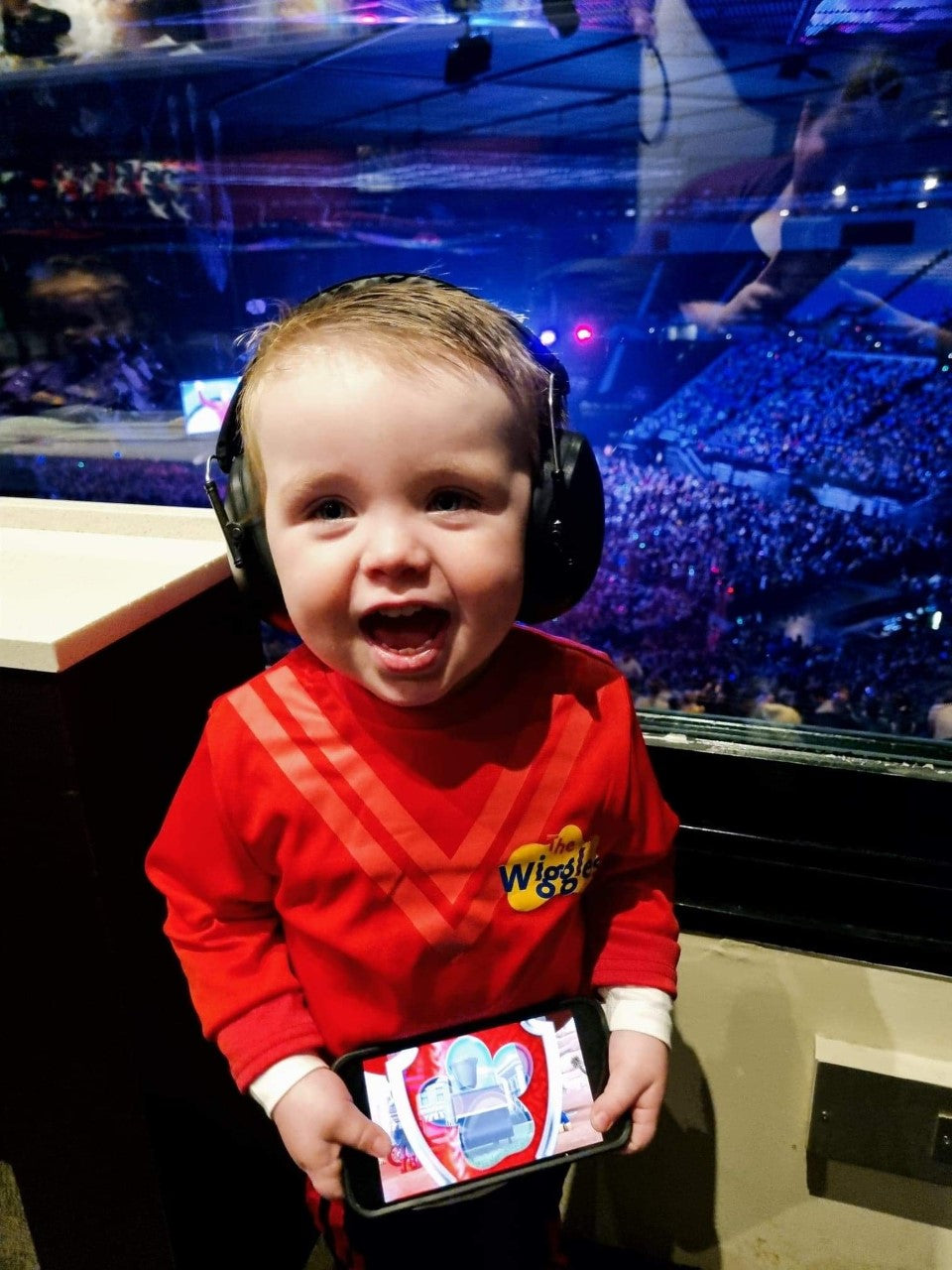 a young boy smiling wearing the Banz noice reduction earmuffs in a red wiggles shirt