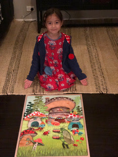 a young girl sitting behind a puzzle smiling