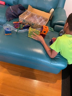 a young boy in yellow shirt plays with his connetix set on a blue lounge