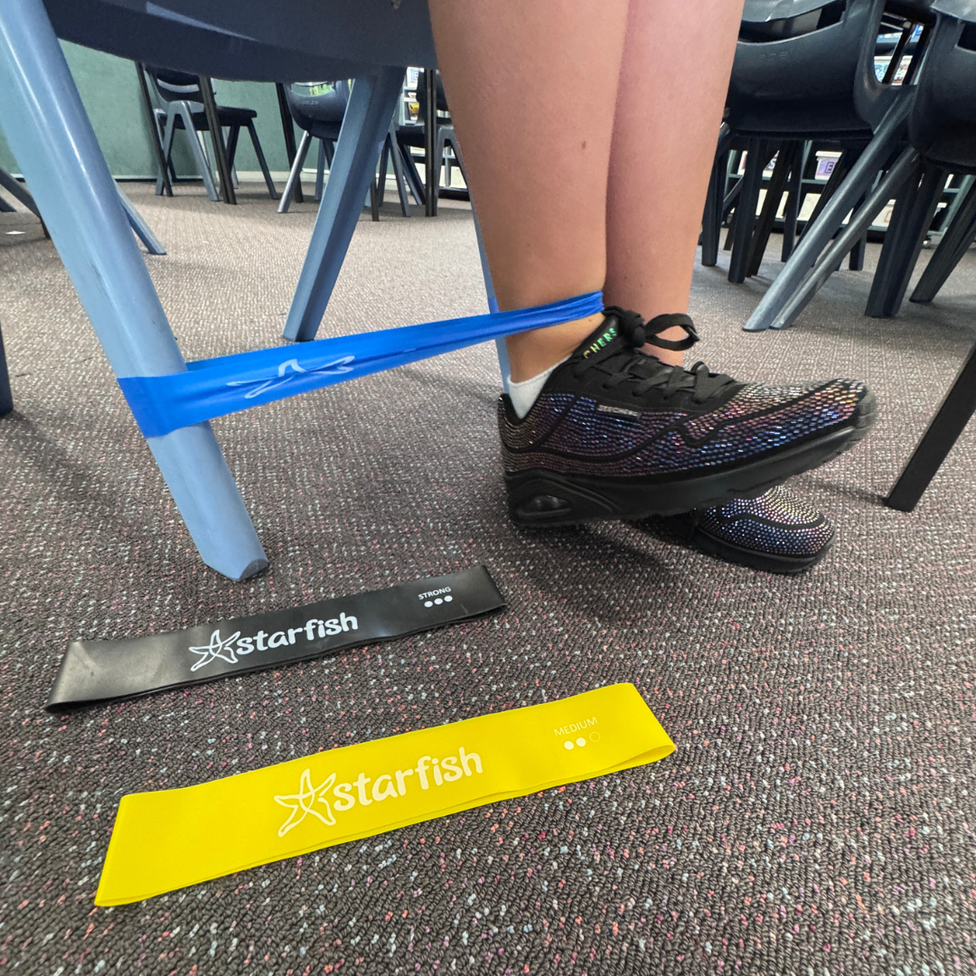 Person using a blue resistance band on a chair with 'Starfish' branding on a carpeted floor.