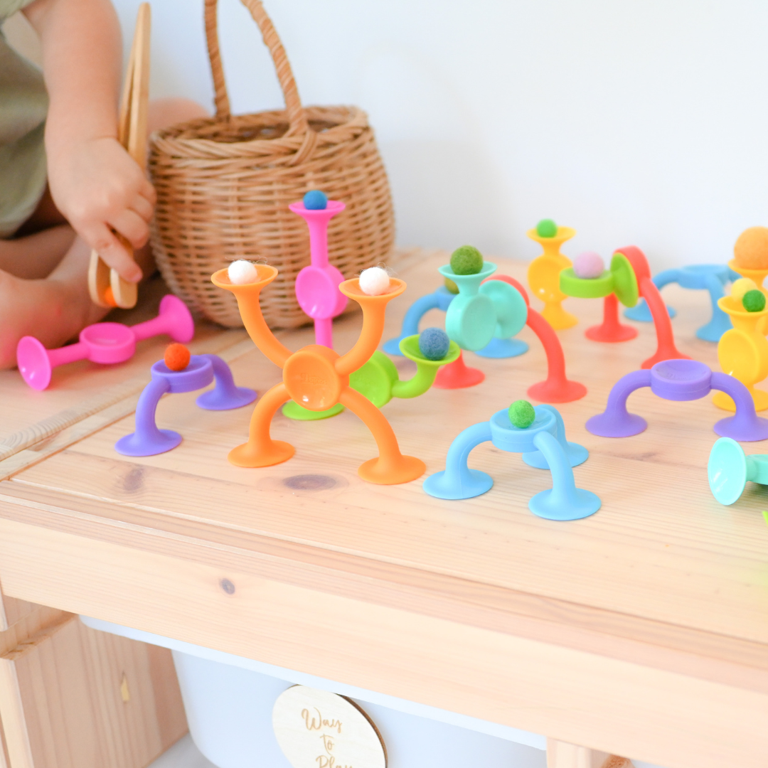 The Fat Brain Squigz stuck to a wooden table while a child is playing with them