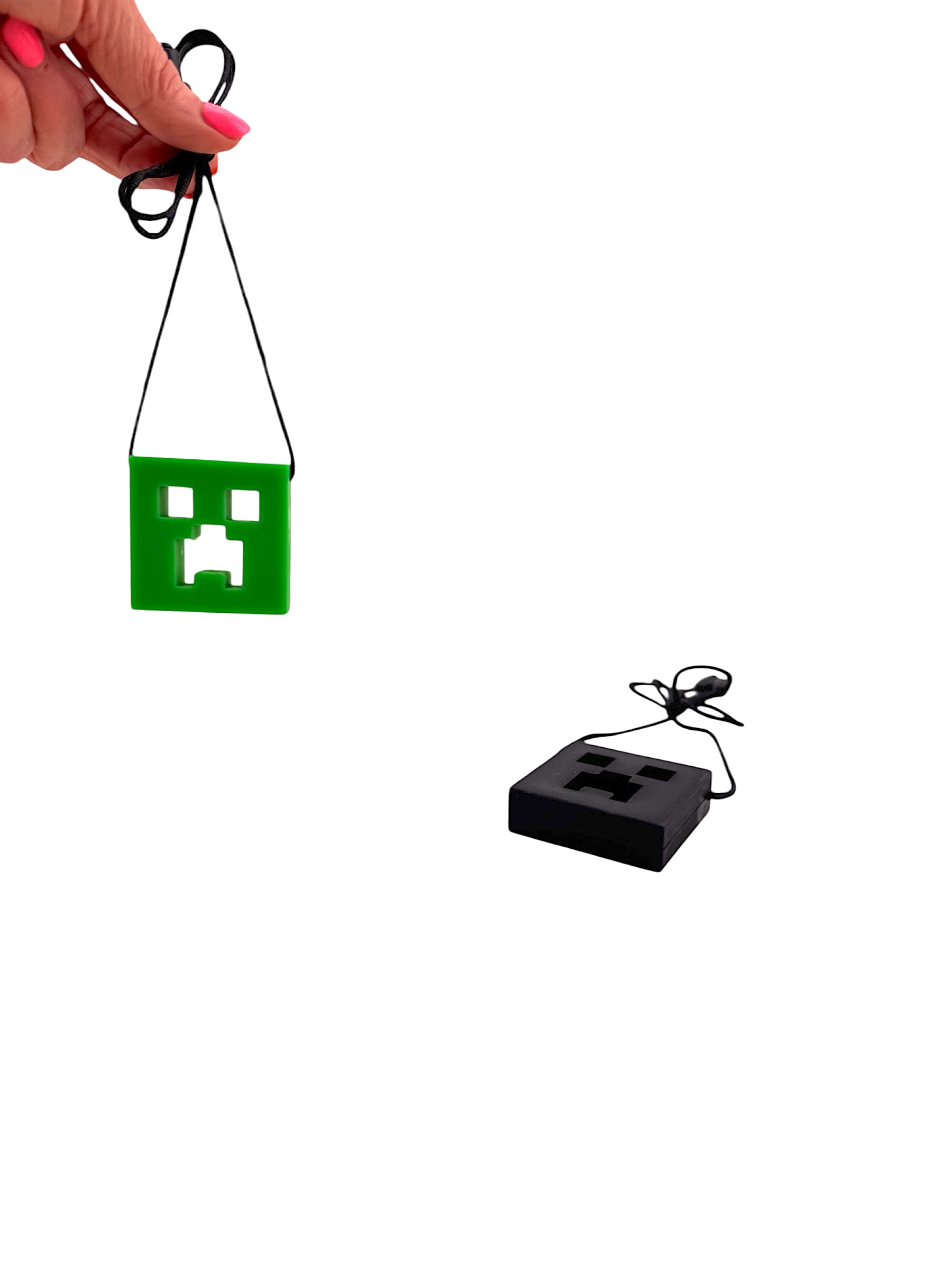 a hand holding the green Chewy Charms Necklace Chew - Creeper in front of the black Chewy Charms Necklace Chew - Creeper