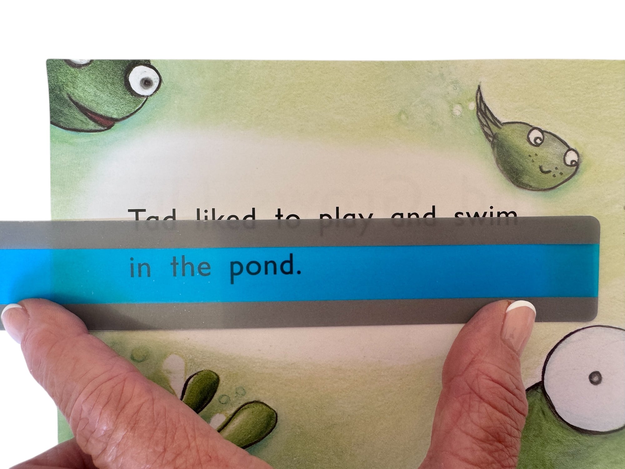 Children's book page with a frog illustration and text, held open by a hand.
