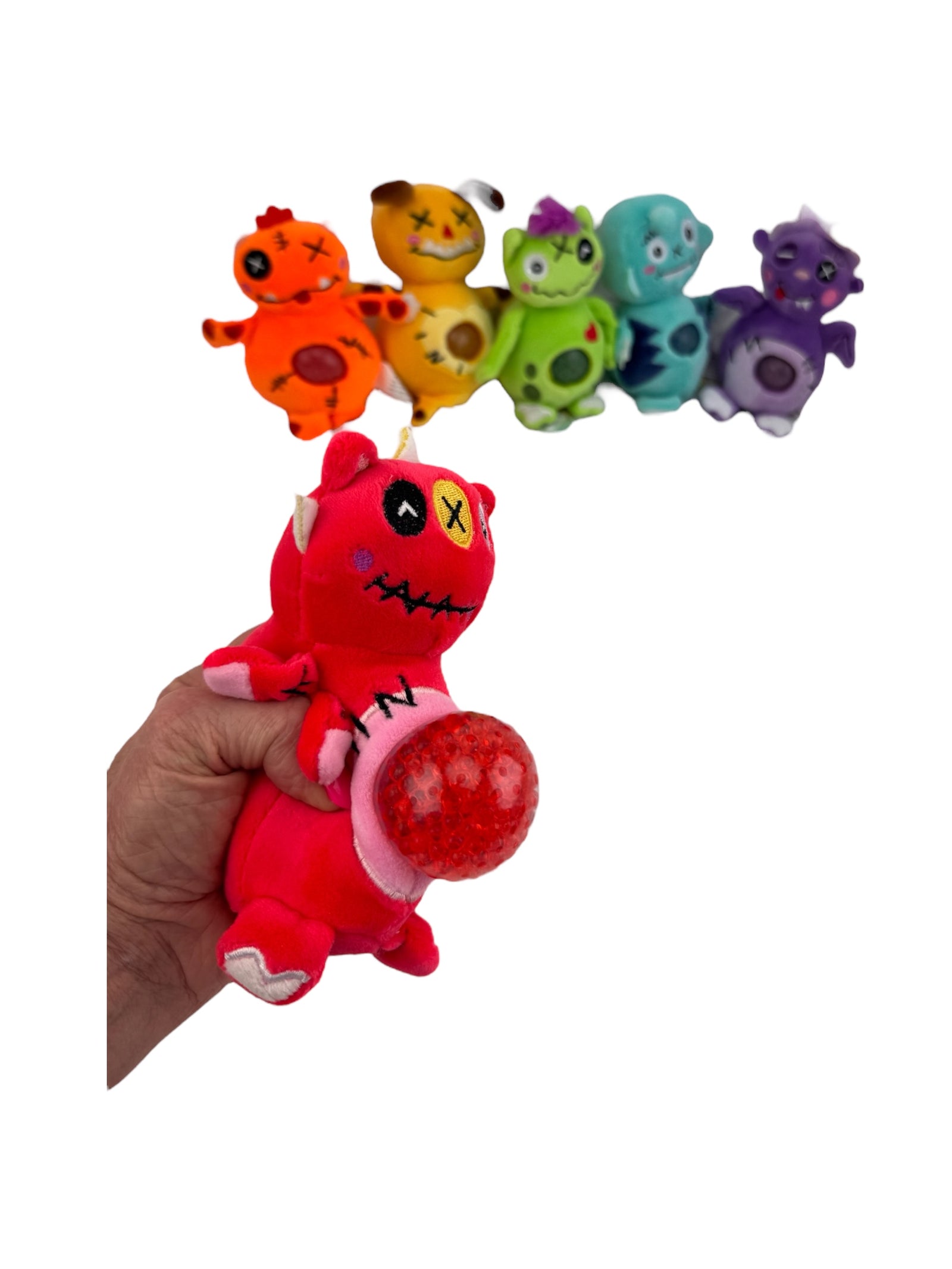 a hand holding the red Jellyroo Monster Stress Ball in front of other colourful toys on a white background