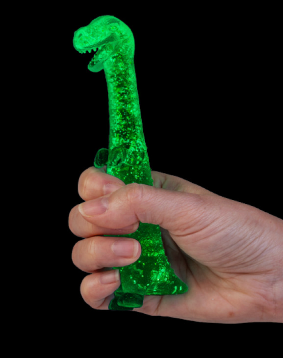 A hand holding the green Smooshos Super Squeeze Glow - Stretch Dino in the dark