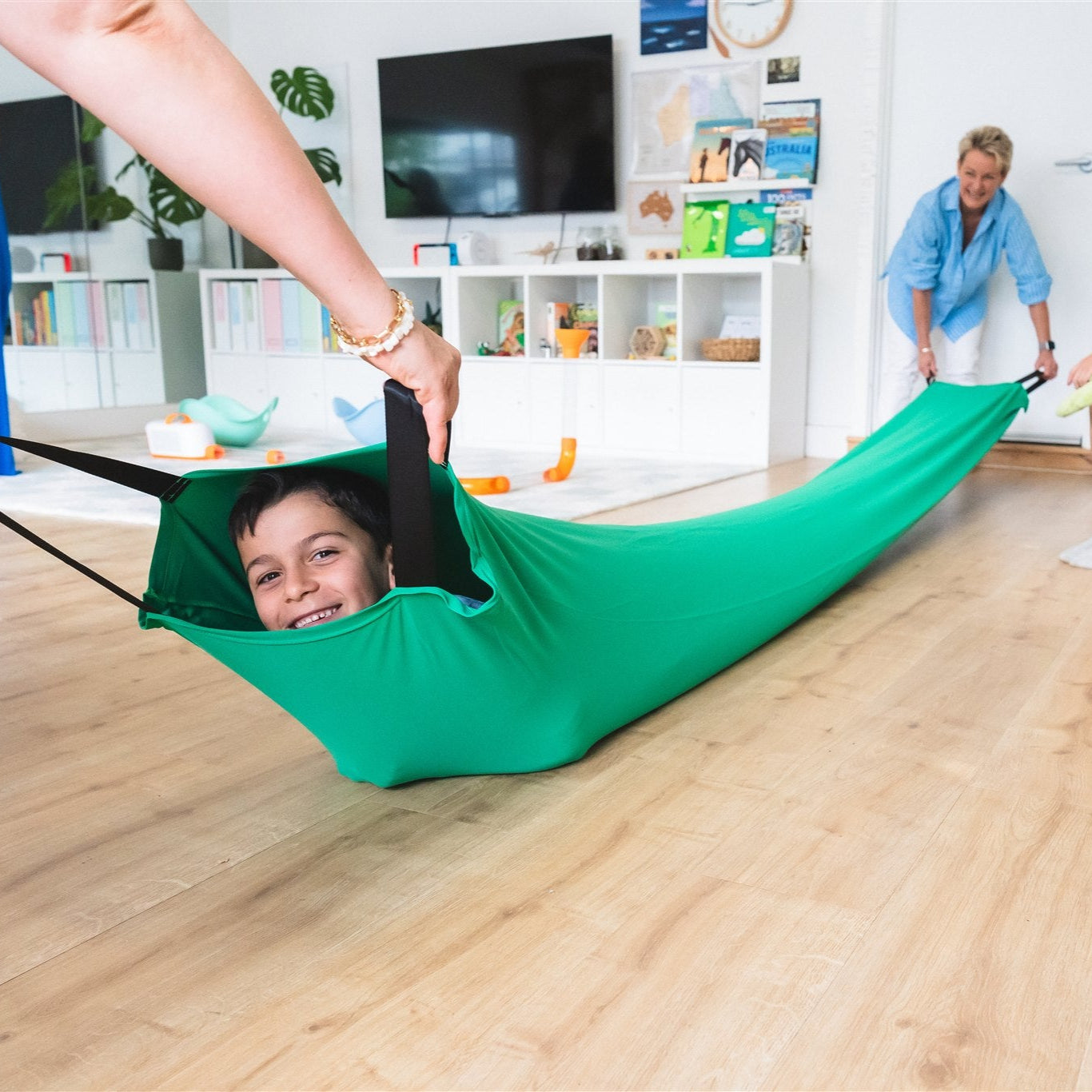 A young boy crawling through the green Deluxe Lycra Compression Tunnel with an older lady in background