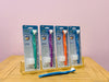 the green, purple, orange and blue Surround Toothbrush - Adult stacked nect to each other with another blue one lying in front on wooden table