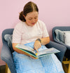 a woman sitting down on a chair with the blue 2.5kg Weighted Lap Pad