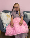 a young girl sitting down on a chair with the pink 2.5kg Weighted Lap Pad