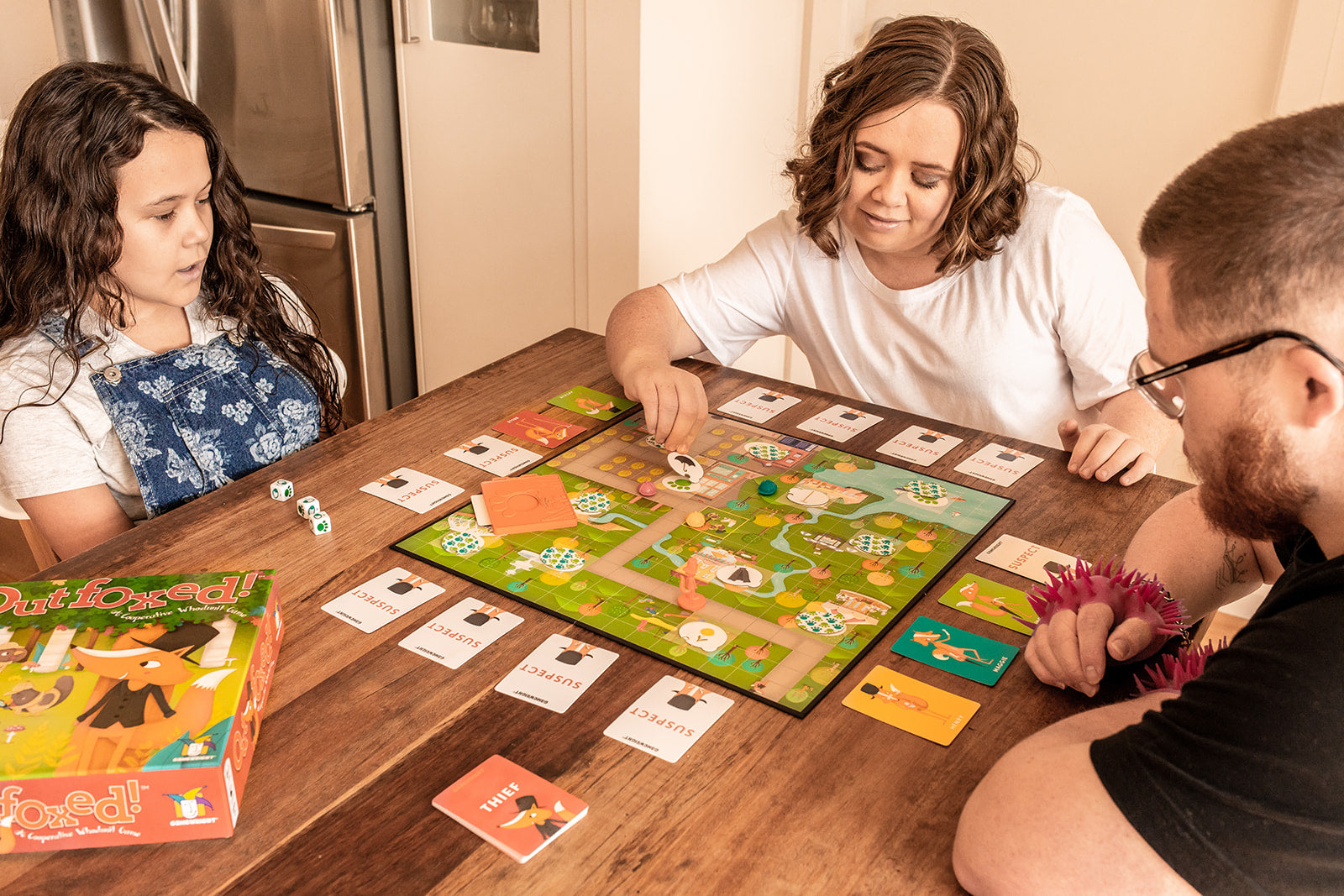 2 girls and a boy playing Gamewright Outfoxed on a wooden table