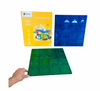 Hand holding green Connetix Tiles Base Plates with blue plate and packaging placed behind it on white background